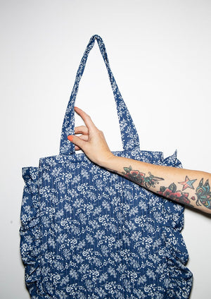 Person holding a blue floral-patterned tote bag against a white background
