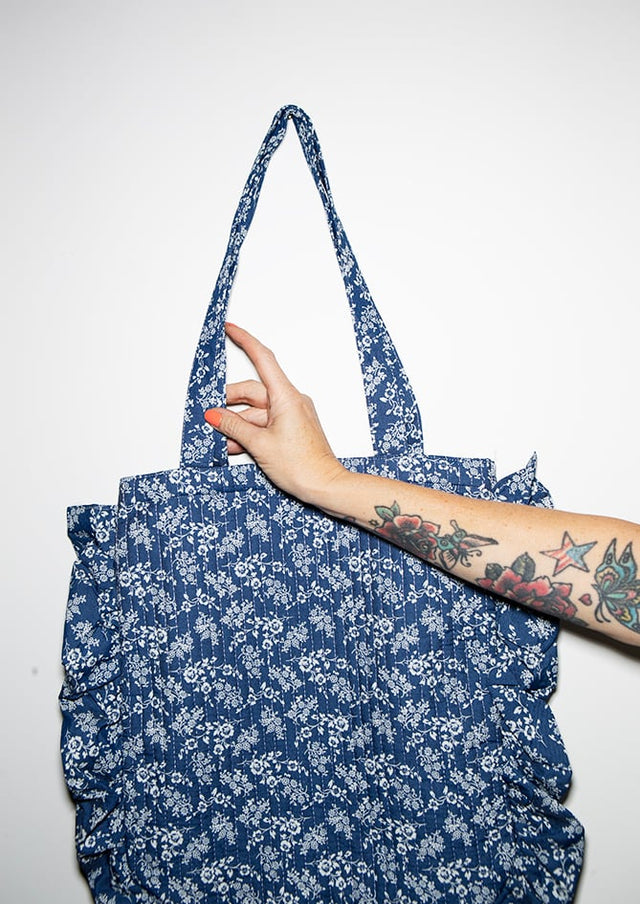 Person holding a blue floral-patterned tote bag against a white background